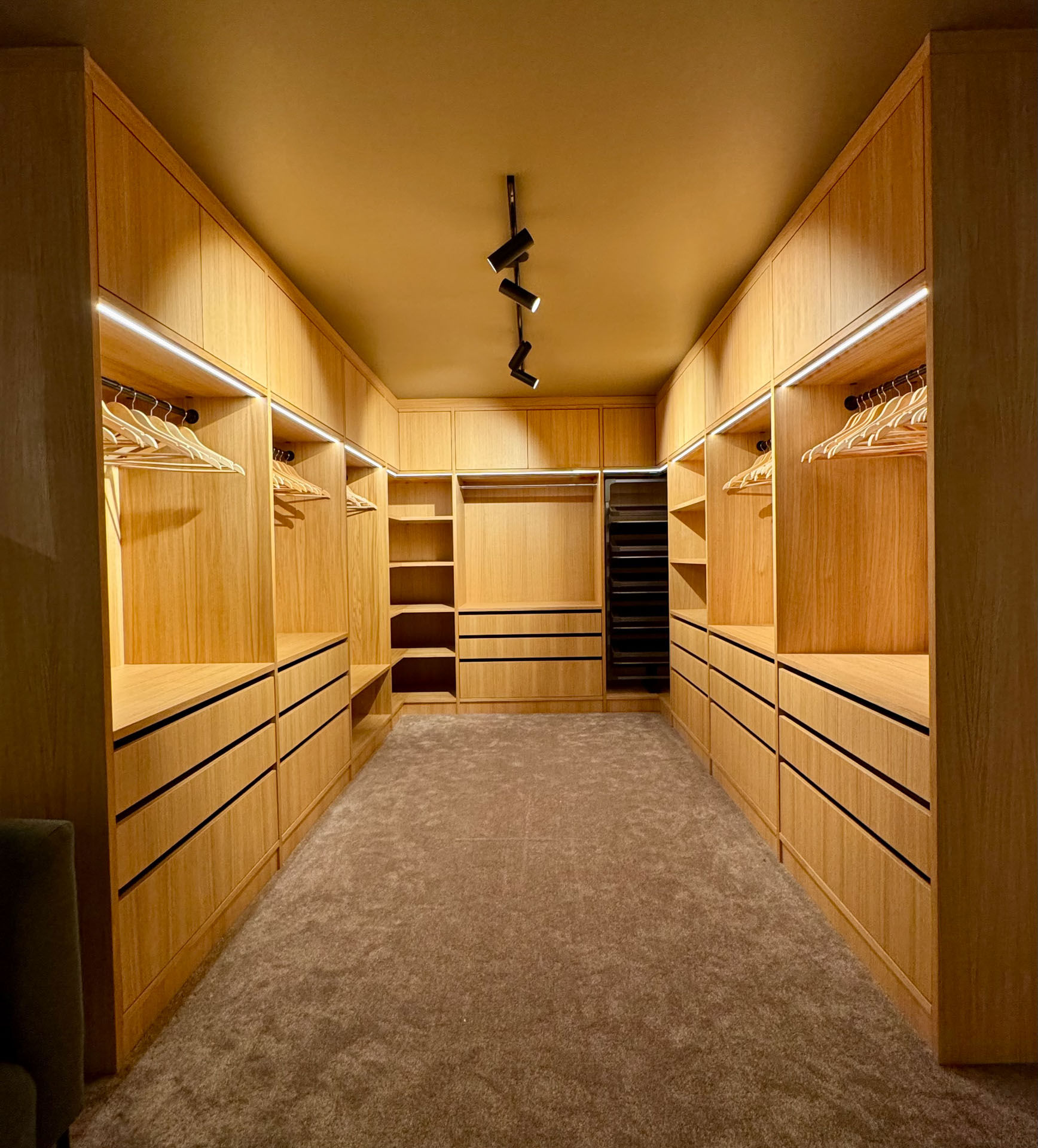 Oversiktsbilde av skreddersydd walk-in garderobe i heltre med integrert belysning, skuffer, hyller og heng