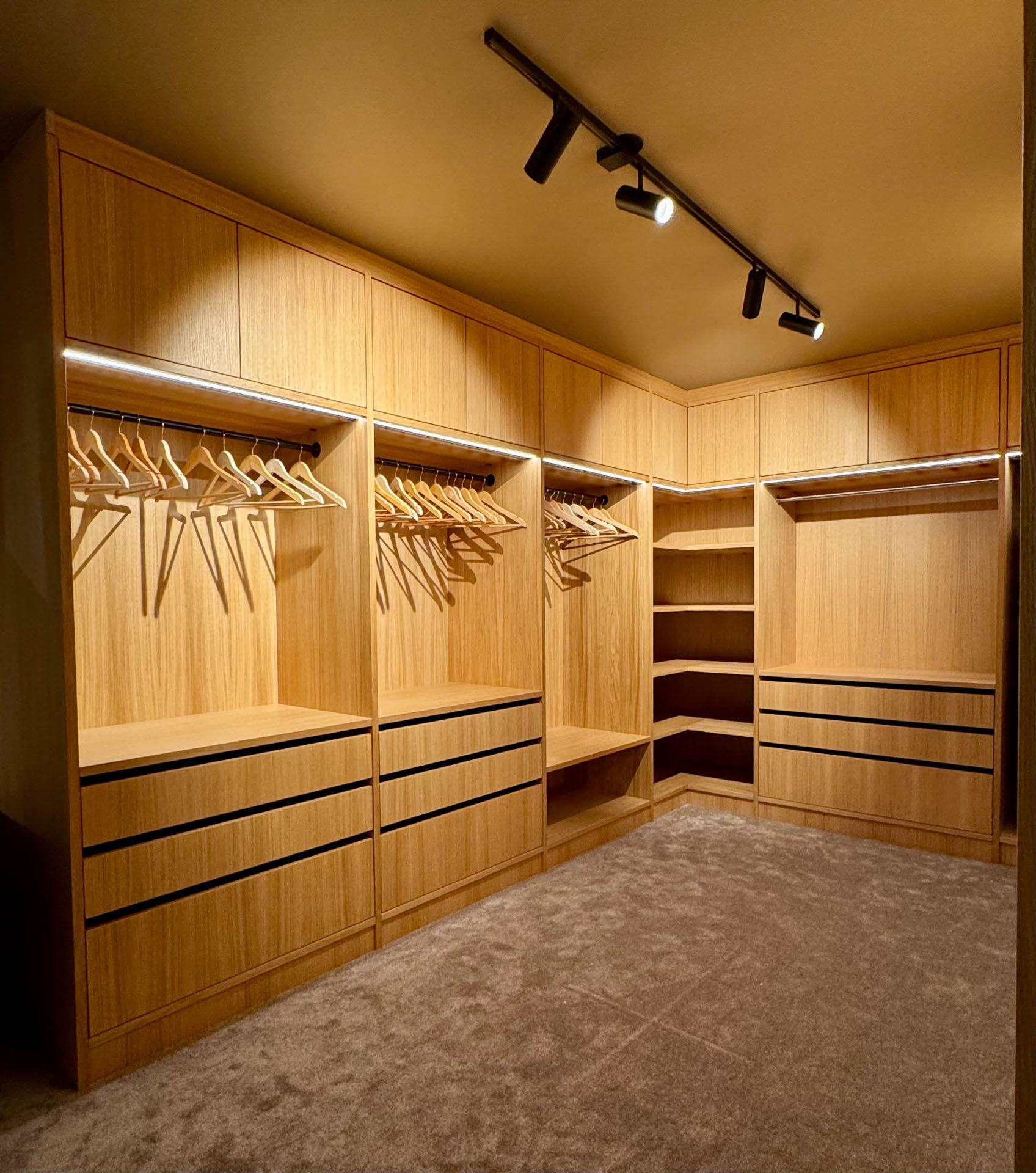 Oversiktsbilde av skreddersydd walk-in garderobe i heltre med integrert LED-belysning, skuffer, hyller og heng