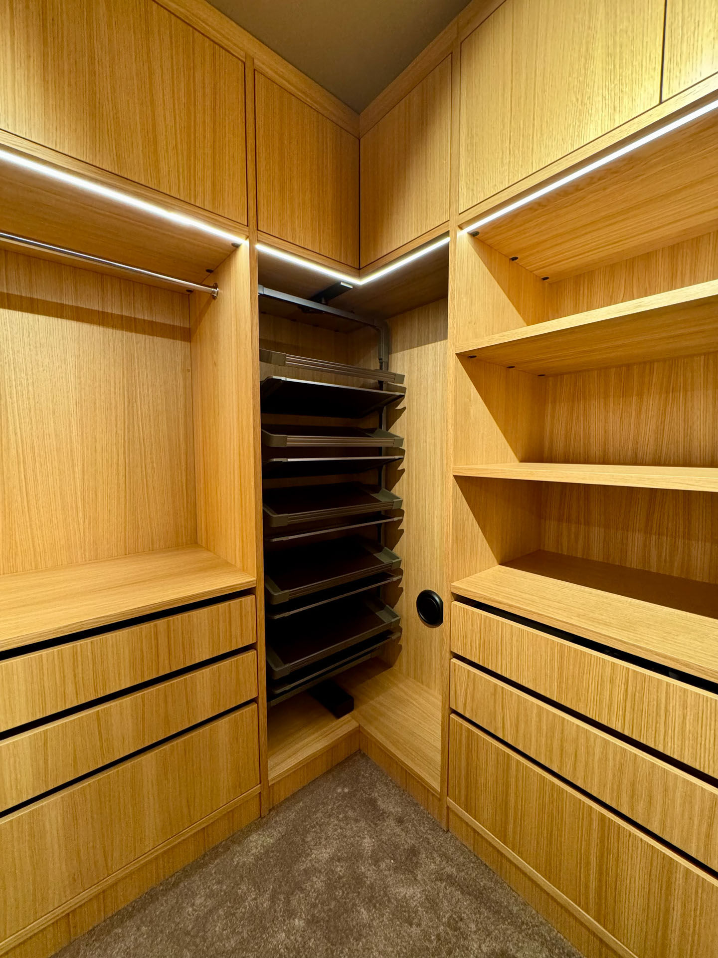 Detaljbilde av skreddersydd garderobeløsning i heltre med uttrekkbare hyller, skuffer og integrert LED-belysning