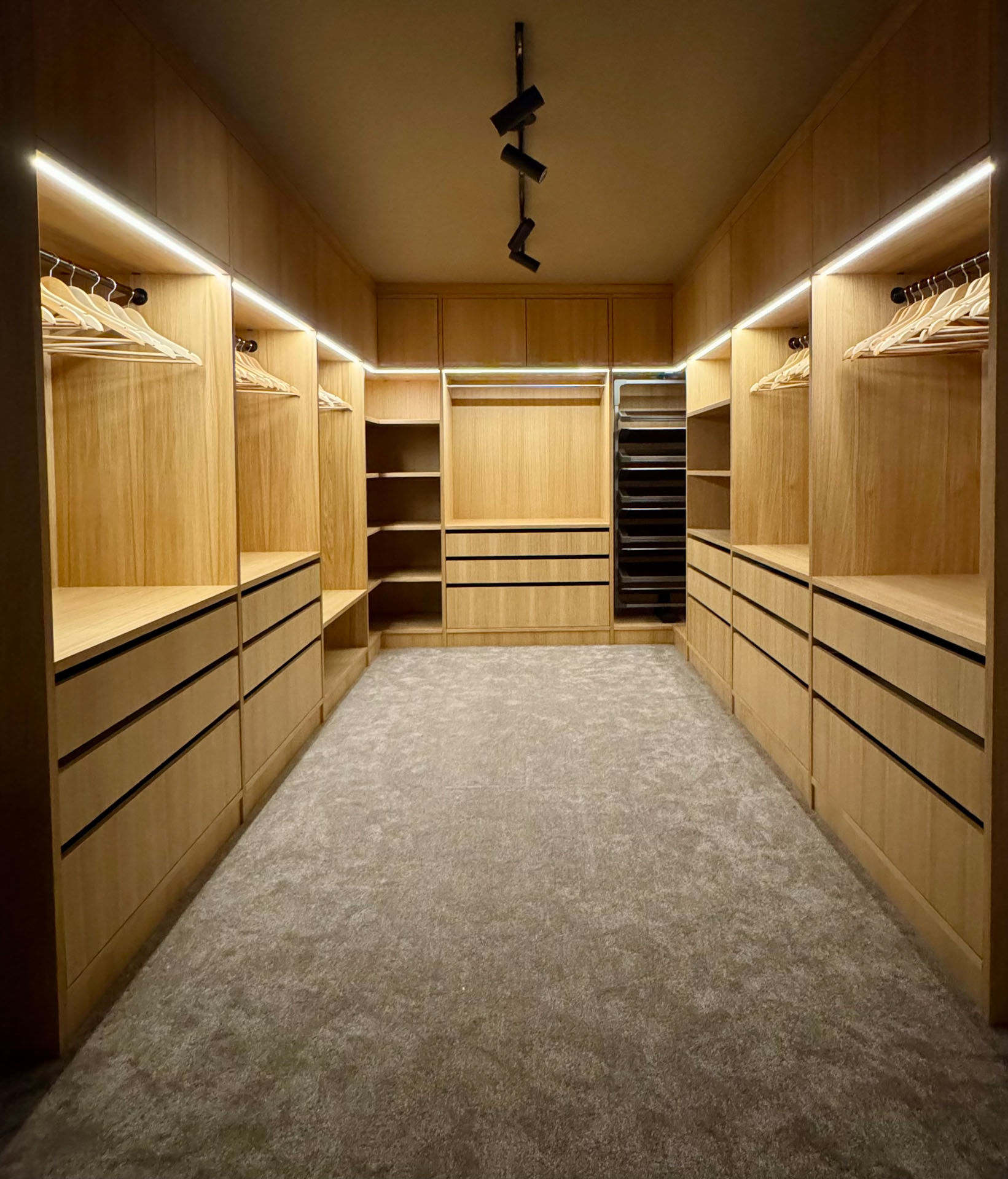 Oversiktsbilde av skreddersydd walk-in garderobe i heltre med integrert LED-belysning, skuffer, hyller og heng