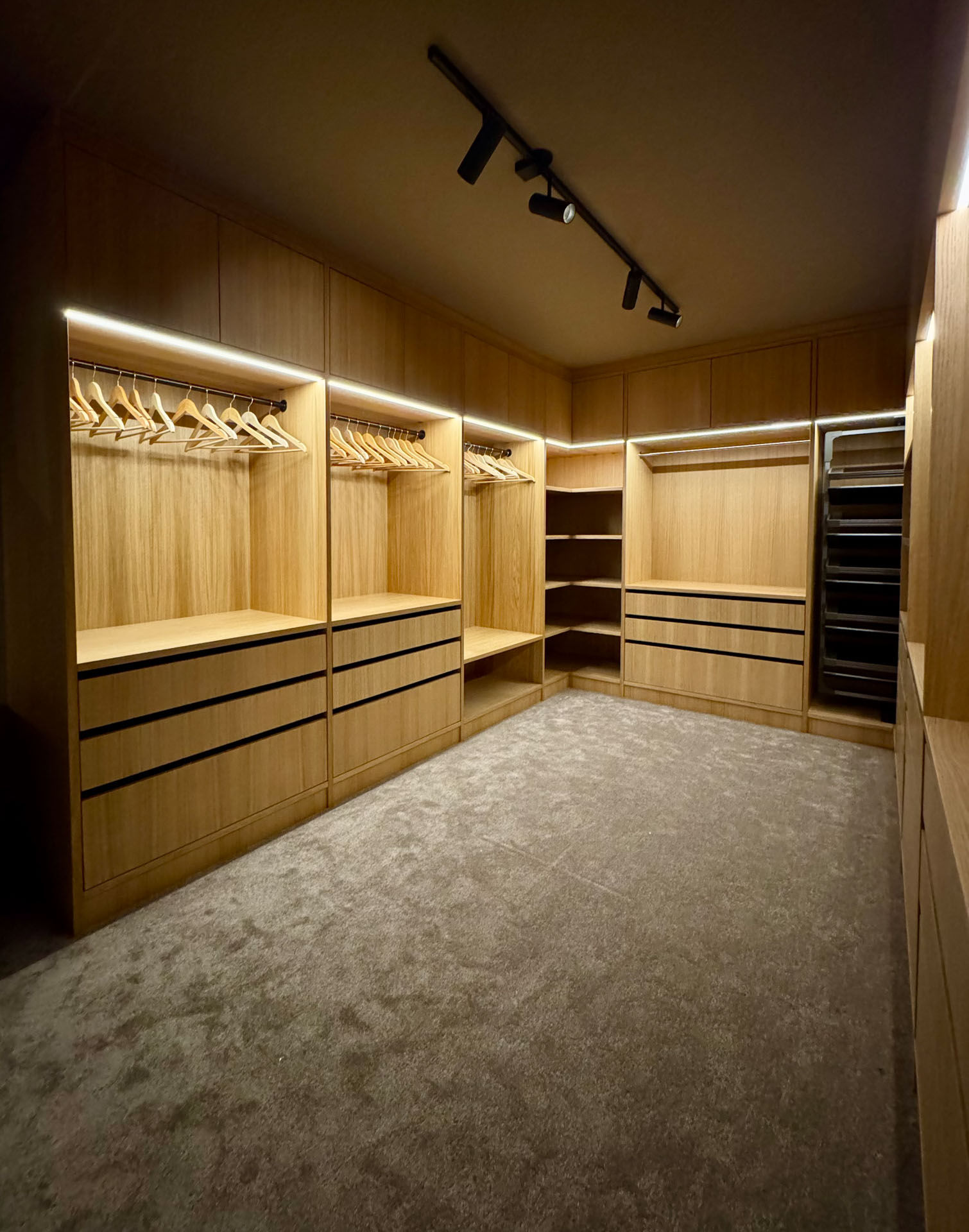 Oversiktsbilde av skreddersydd walk-in garderobe i heltre med integrert belysning, skuffer, hyller og heng