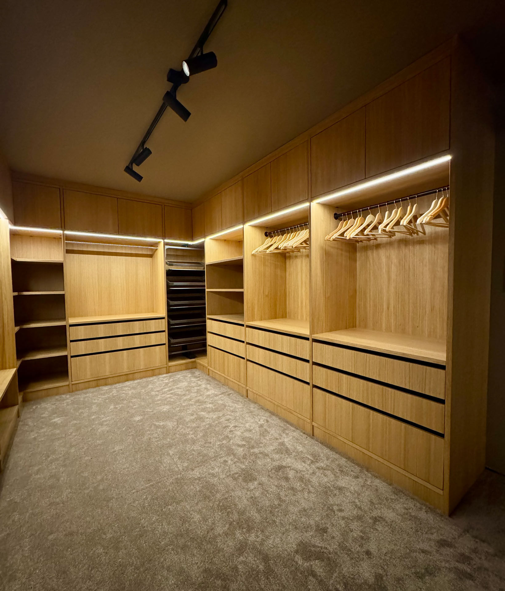 Oversiktsbilde av skreddersydd walk-in garderobe i heltre med integrert LED-belysning, skuffer, hyller og heng