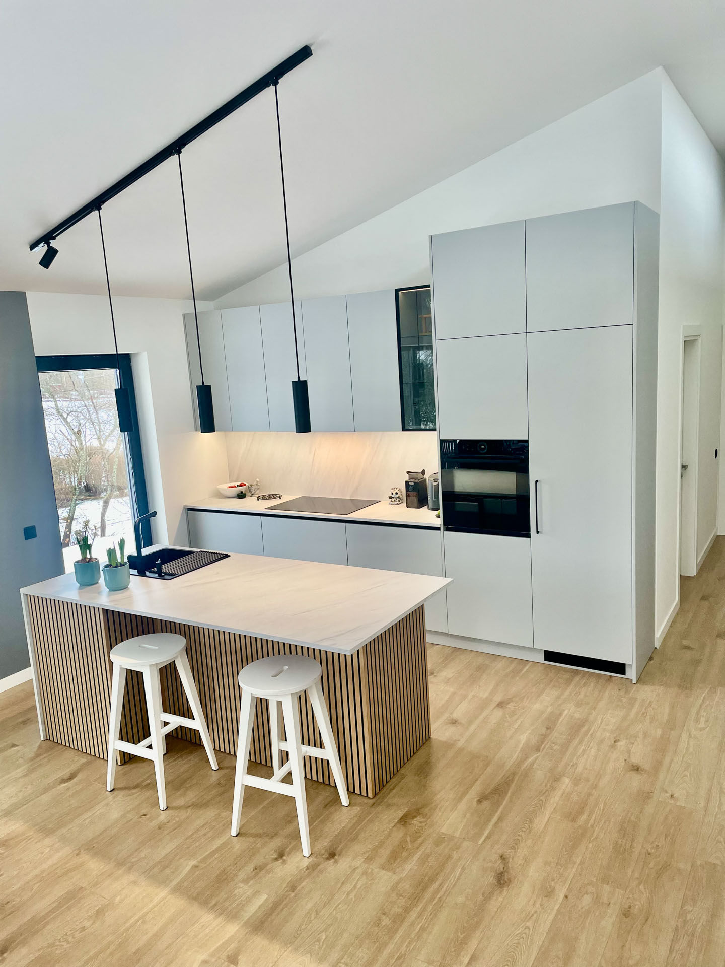 Moderne kjøkken med lyse fronter, kjøkkenøy i tre og steinbenkeplate i åpen løsning