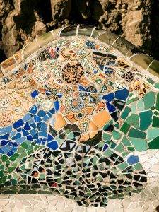 Közelkép a Park Güell egyik hullámzó padjáról, amely a kék, zöld és okker színű törött kerámiákból összeállított trencadís mozaiktechnikát szemlélteti.
