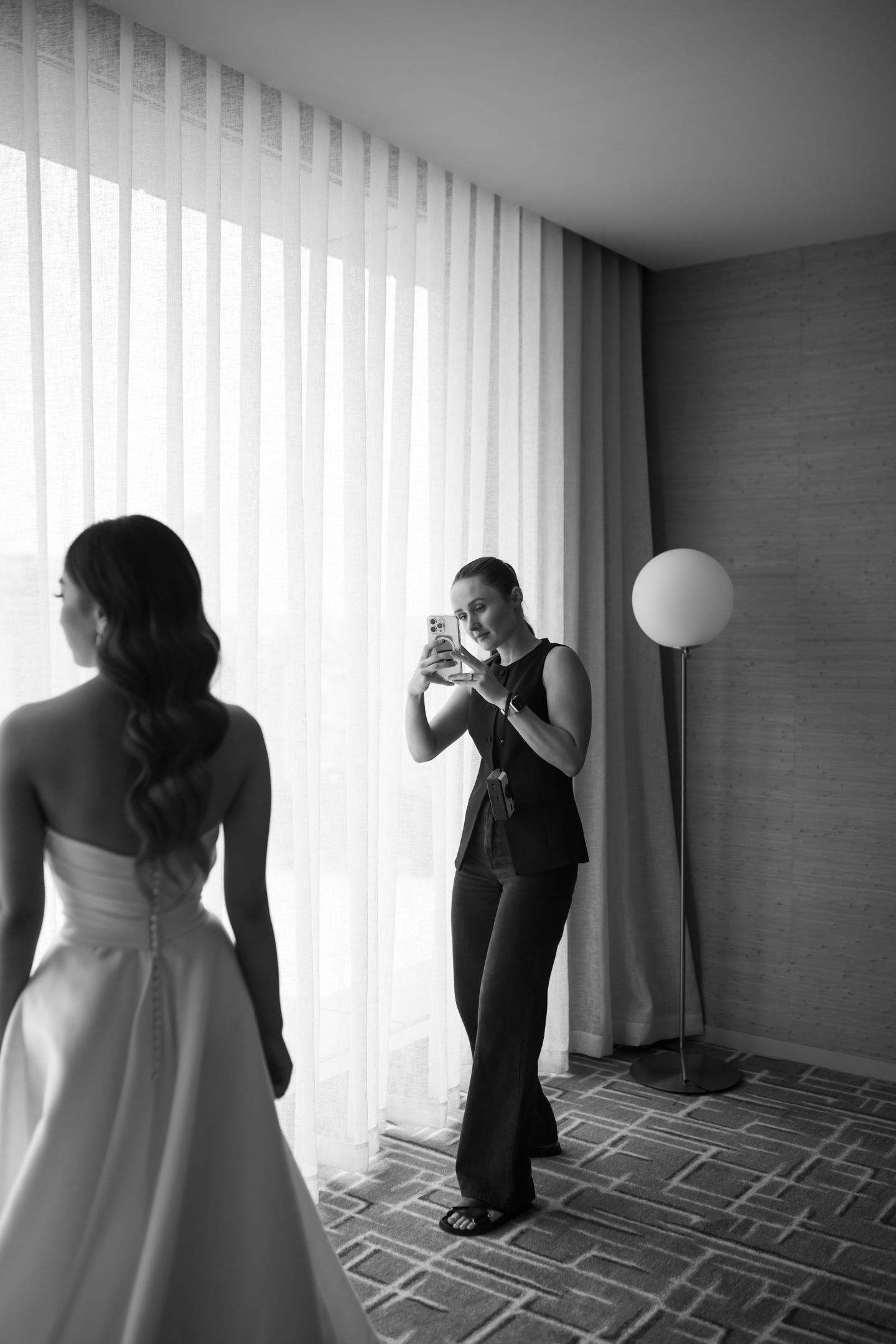 Black and white photo showing a wedding content creator capturing a bride on her iphone.