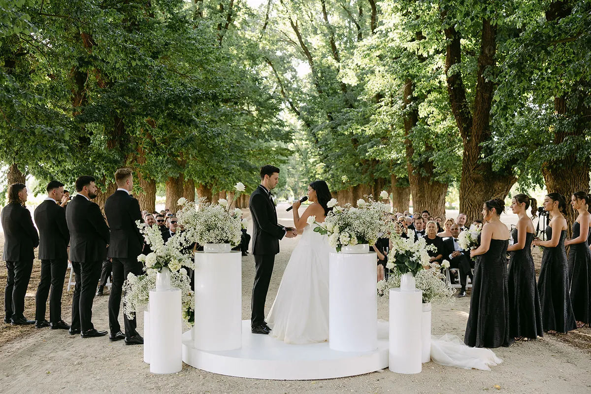 A wide shot of a wedding ceremony from behind the couple, with bridal party in black.
