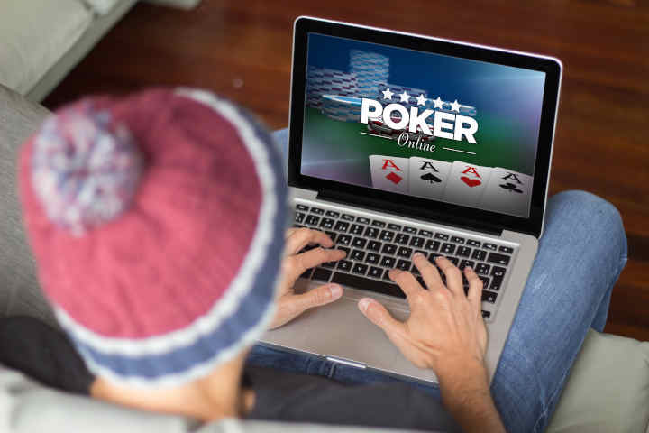 Playing cards and poker chips arranged on a table, with a laptop in the background showing an online poker game.