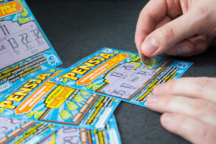 A hand holding several used scratch-off tickets.