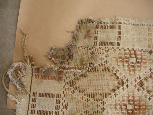An antique carpet with dry rot before repair.