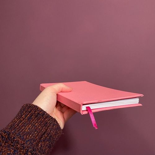 A pink handmade notebook, help at an angle so you can see the pages from the bottom, but still see the front cover.