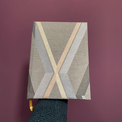 A grey handmade notebook with gold crosses. It is textured like wallpaper.