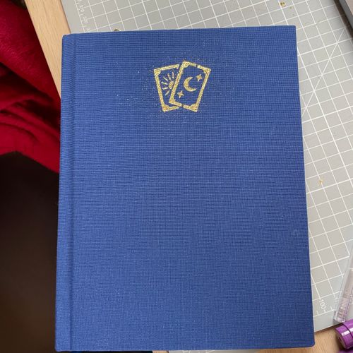 A blue handmade book with gold foiling that depicts two tarot cards.