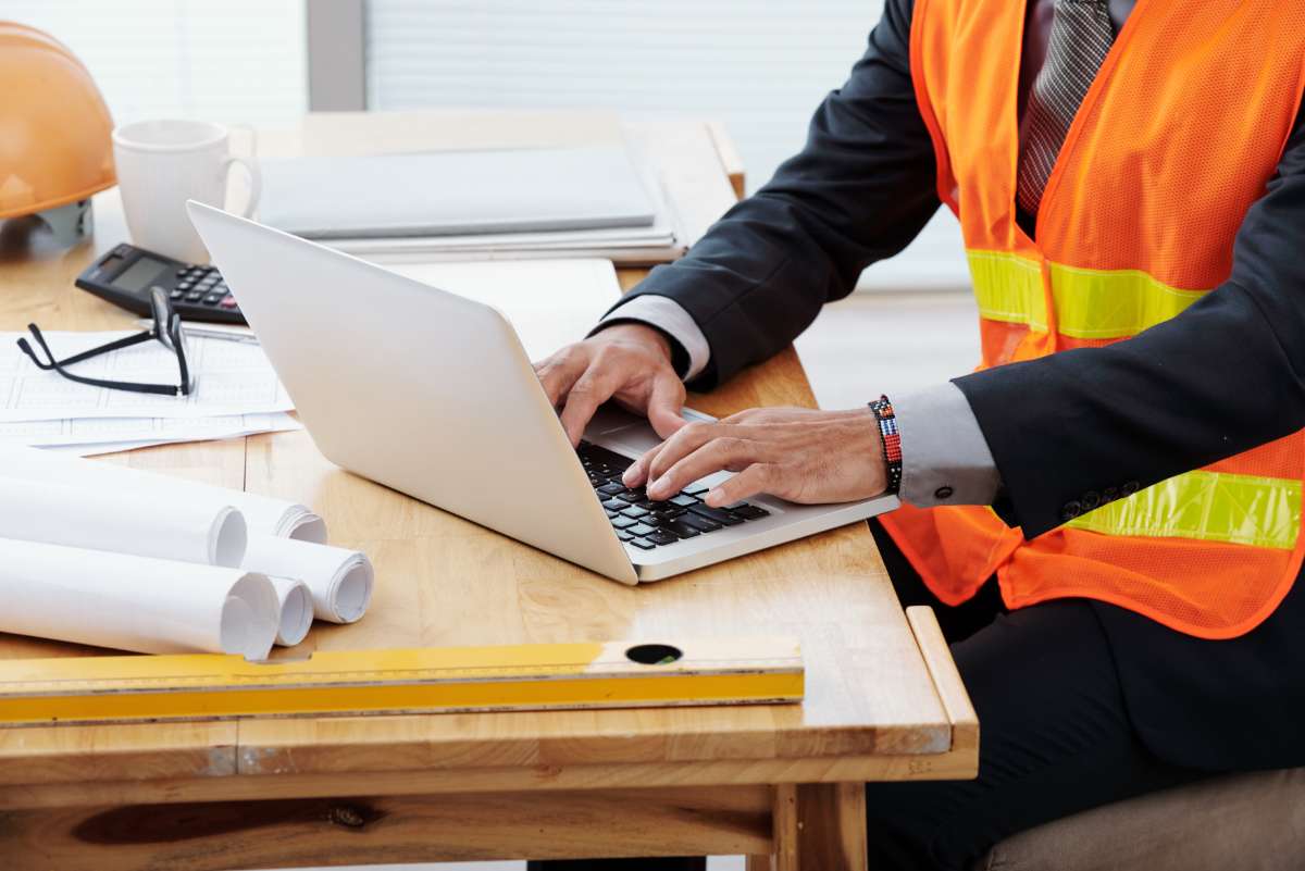 man in neon safety vest high vis and business suit sitting at desk using laptop in GIS career