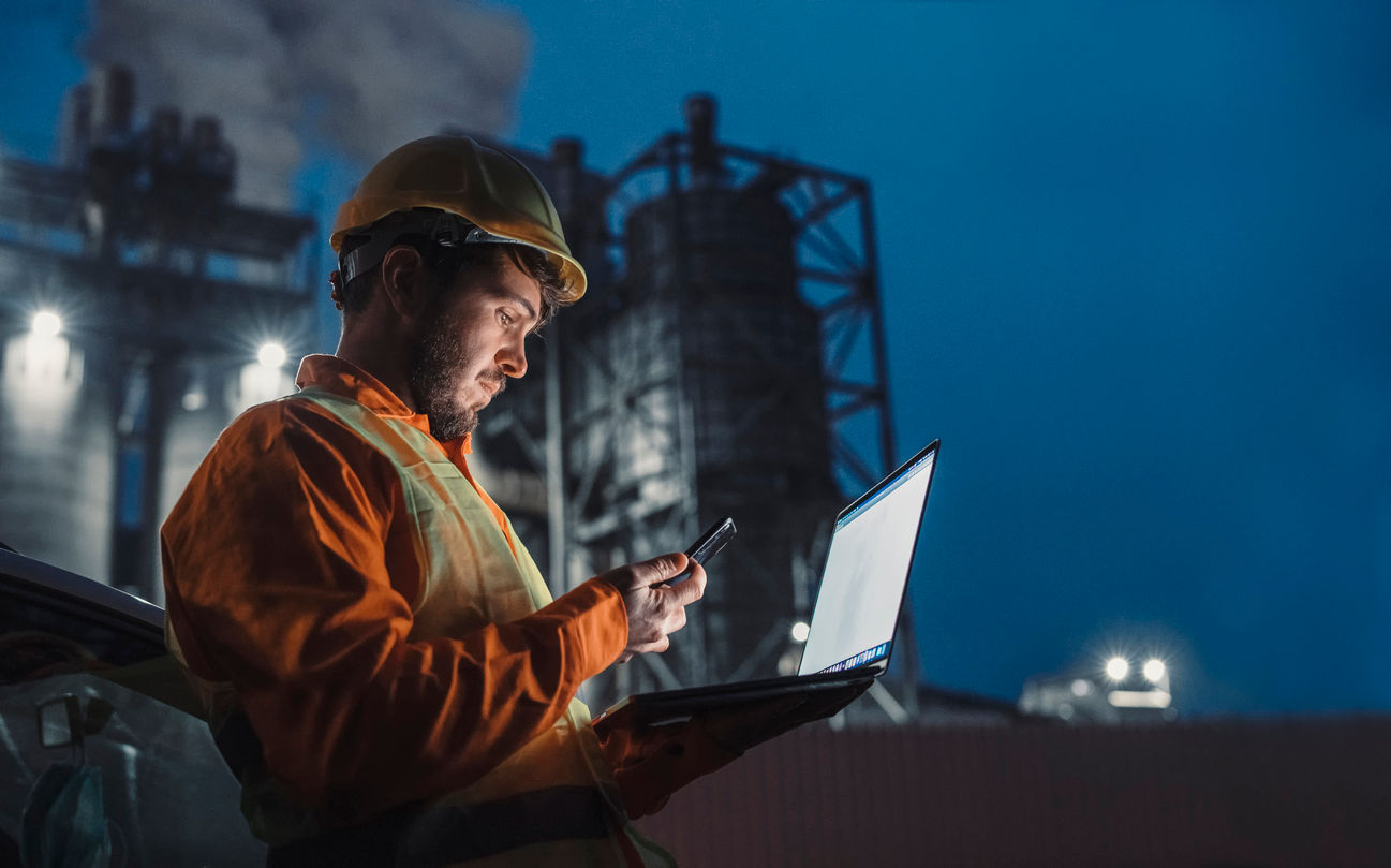 Male oil industry worker checking reports and data using field service management software on a laptop.