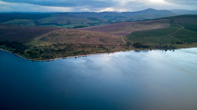 Aerial view at dusk of a water reservoir, green meadows, and distant mountains