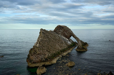 Natural sea arch Bow Fiddle Rock at evening with a vibrant sky in the distance.