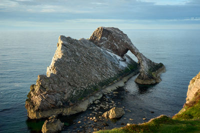 Natural sea arch Bow Fiddle Rock at dusk, with a colourful sky in the background.