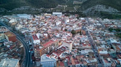 Aerial view of a Spanish city with bustling structures and a blue building at the center. Vineyard and mountains in the distance.