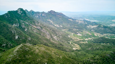 Aerial view of mountainous region. Panoramic valley view from towering peak at center, surrounded by mountain peak, valley and trees. Majestic nature.