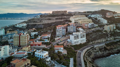 Aerial view of coastal town on cliff, overlooking ocean. Shows additional cities on hillsides and house on cliff. Explores diversity of coastal living.