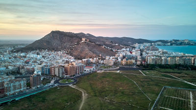 Bird's-eye view of Cullera, Spain with mountains as backdrop. Panoramic shots from hilltops show city and ocean, aerial view of diverse architecture and bustling streets, and park overlooking city.