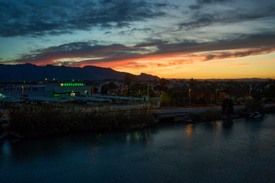 Cullera, Valencia, Spain - 03.13.2023 Sunset over a tropical city nestled against majestic mountains. Serene ambiance as palm trees sway and people gather by the calm waters.