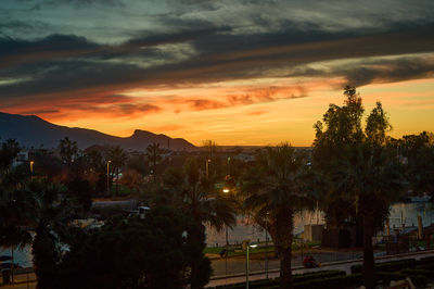 Cullera, Valencia, Spain - 03.13.2023 Sunset over a tropical city nestled against majestic mountains. Serene ambiance as palm trees sway and people gather by the calm waters.