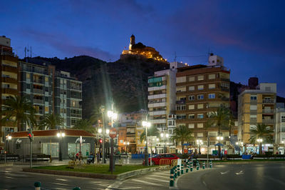 City lights illuminate the urban landscape as a majestic mountain overlooks the bustling metropolis. A striking contrast of nature and city life defines this captivating Cullera, Spain scene.