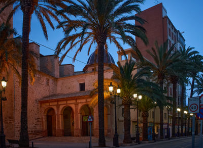 Cullera, Spain 05.21.2023 Urban Street at Dusk: Grand building surrounded by palm trees, creating a balanced and inviting composition.