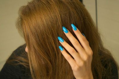 A hand with a blue manicure touching brown hair