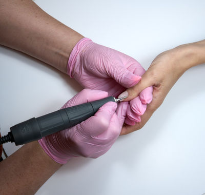 During a manicure, a manicurist buffs off nail polish with an electric nail file. Close up