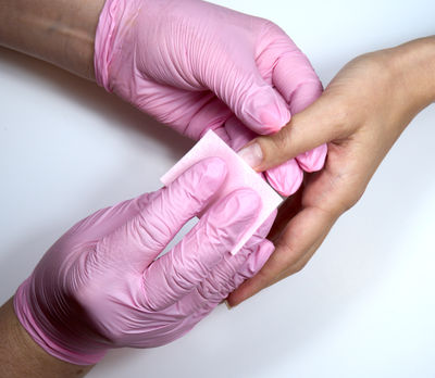 A manicurist is using a tissue to clean a client's nails.