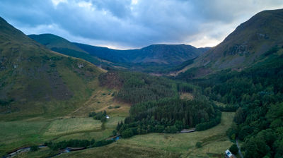 An aerial view of Glen Doll - mountains, pine forest and a river under evening sky