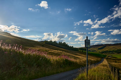 Glen Quaich in Scotland has a road, a road sign, verdant farmland, and a woods under a clear sky.