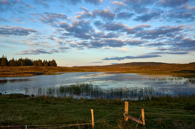 Evening over Scottish landscape with a small loch, forest, and hills under colorful sky