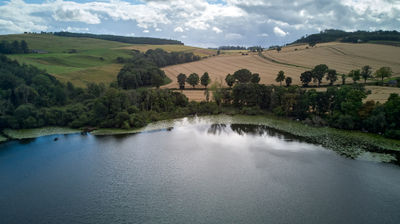 An aerial view of a Scottish loch and green trees and yellow fields