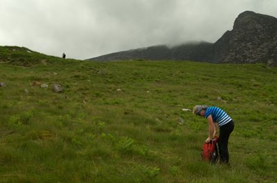 Isle of Arran, Scotland. A serene landscape with rolling green hills and a misty mountain range in the distance. A couple walks leisurely, blending into the peaceful surroundings.