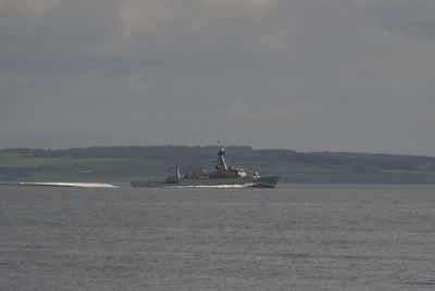 Isle of Arran, Scotland. An image captures a serene scene with a ship cruising on calm waters, reflecting vividly. A cross stands tall against the dramatic sky, conveying tranquility and vastness. A.