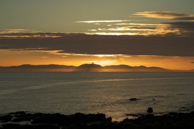 Kintyre, Scotland. A serene sunset over the ocean with wispy clouds, vibrant colors, and a small boat creates a tranquil and beautiful ambiance.