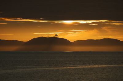 Kintyre, Scotland. A stunning sunset paints the sky with vibrant colors, contrasting against the mountains. Tranquil waters reflect the ethereal atmosphere, creating a serene and beautiful scene.