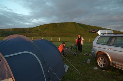 Kintyre, Scotland. A serene camping site in the countryside surrounded by green hills, colorful tents, a sleek car, and a close-up of natural elements creates an inviting scene for outdoor enthusiasts