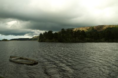 A serene scene with a boat on calm water, surrounded by mountains, trees, and clouds, exudes peace and natural beauty.