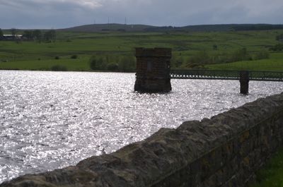 A picturesque scene: stone bridge over glistening lake, mysterious building, green field, blue sky, white clouds. Nature's beauty and human-made structures in harmony.