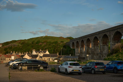 An evening in Scotland with parked cars, a viaduct, and a green hill at a distance