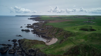 A coastal aerial view - sea, rocks, green shores and a blue sky