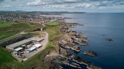 A drone photo of a rocky seaside with a Scottish town at a distance