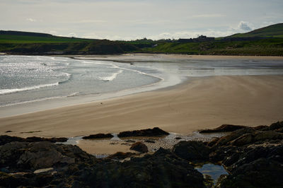 Evening sky over a beach, surrounded by rocks and green shores