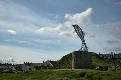 A wire sculpture of a dolphin on a small green hill in a Scottish coastal town