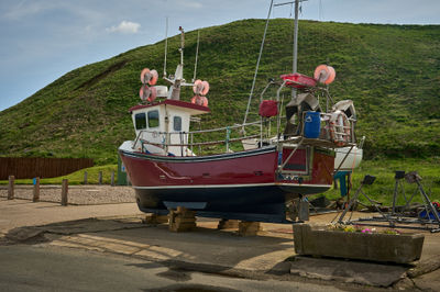 A small red fishing boat ashore with a green hill in a background
