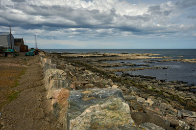 A sea view from a small rocky beach with rocks in the foreground and some buildings at a distance